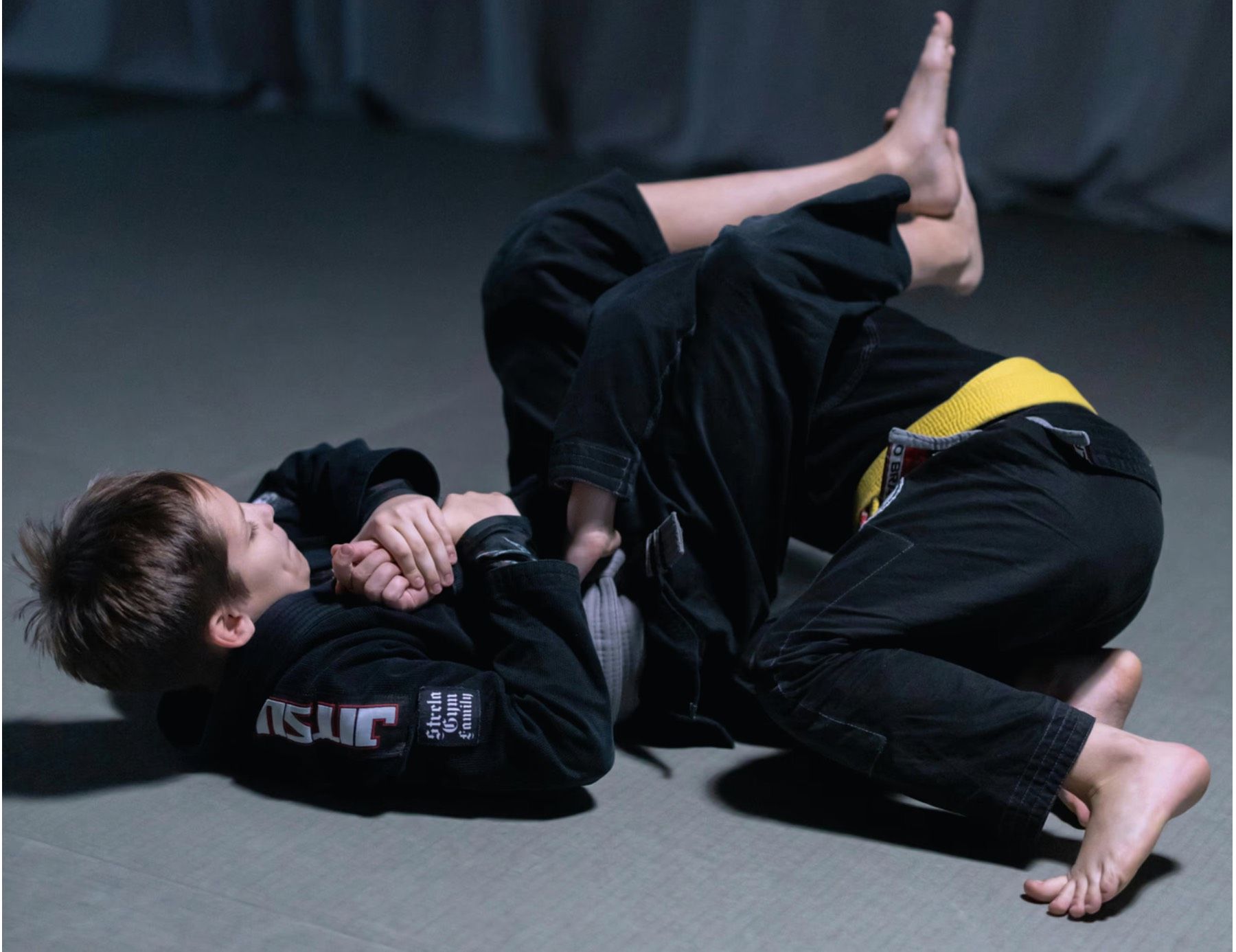 Children in BJJ gi practicing techniques on the mat at a martial arts academy