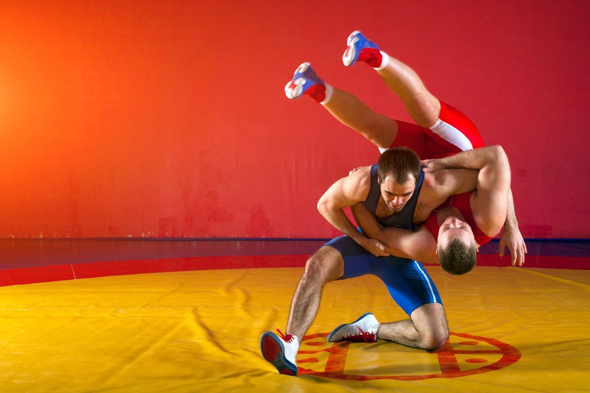 Two wrestlers practicing a throw on a wrestling mat